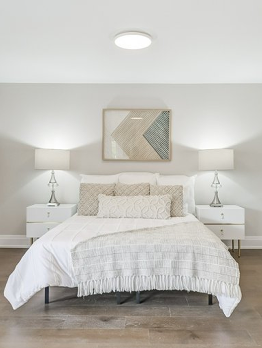Calm bedroom with queen size bed and side tables with lamps on the them and painting on the wall