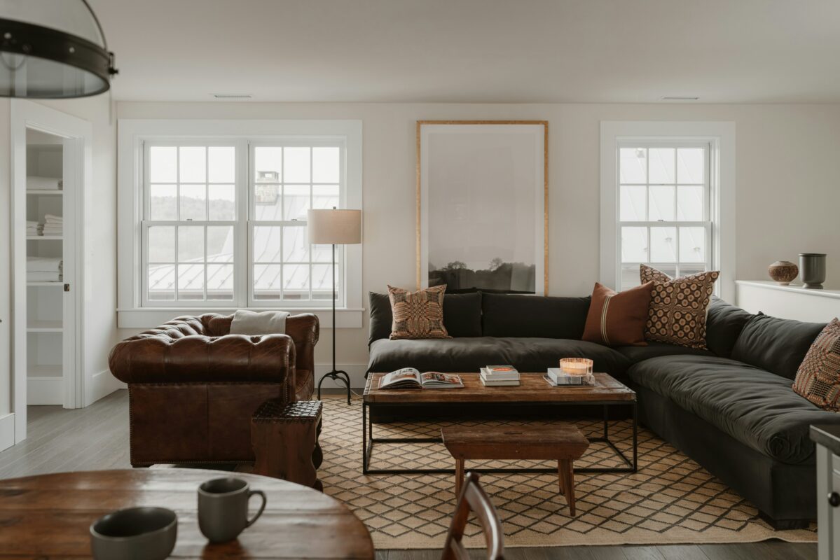 Cozy living room seating arrangement with a black L-shaped sofa and leather accent chair around a wooden coffee table with decorative accents