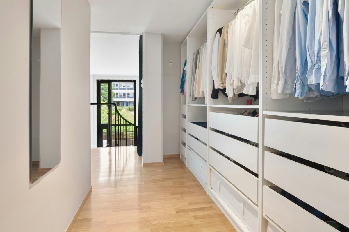 Modern walk-in closet with white shelving and light wood floors.
