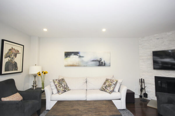 White living room with a white couch and painting and flowers on a side table with a lamp