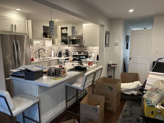 Cluttered kitchen with objects on counter and floor with empty storage boxes