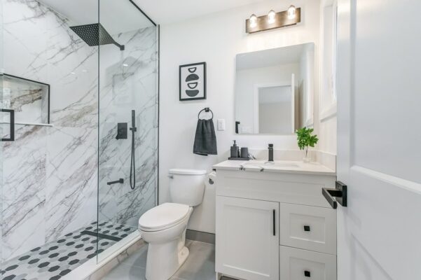 Marble shower, white vanity with black fixtures, and abstract wall art.