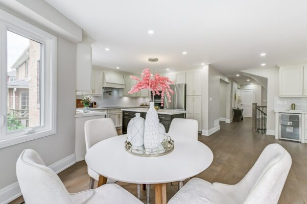 White kitchen with round dining table, pink floral centrepiece, and stainless appliances.