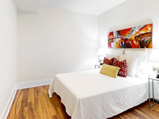 White bedding with red and yellow pillows and bold abstract artwork.
