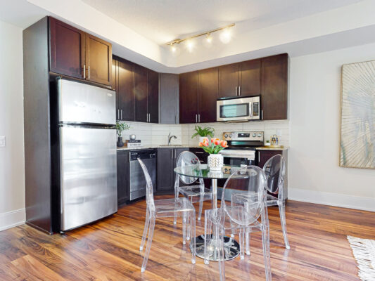 Dark wood kitchen with stainless appliances and round glass dining table.