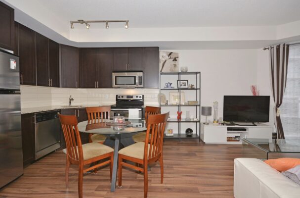 Open-plan kitchen and living area with dark cabinets, glass dining table, and white sofa.