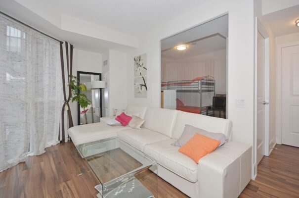 Living room with white sectional, colorful throw pillows, and sheer curtains over large windows.