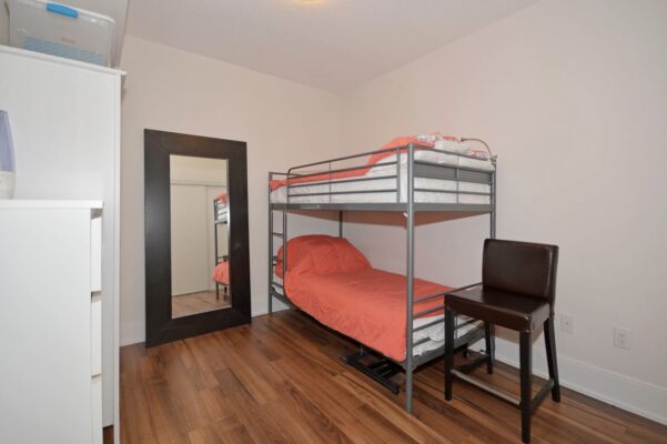 Compact bedroom with metal bunk bed, orange bedding, and full-length mirror.