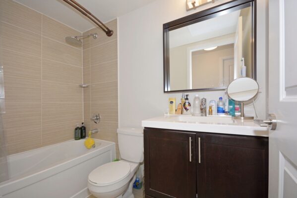 Bathroom with beige tile, bathtub with rainfall shower-head, dark vanity, and large mirror.