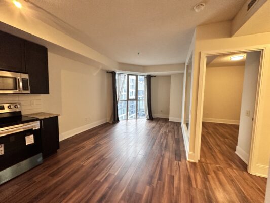 Open layout with dark kitchen cabinets and corner window panels with curtains