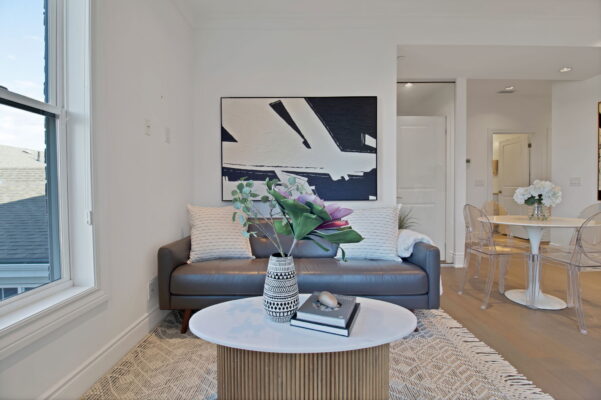 Grey couch and coffee table with plants and books on top and a abstract painting on the wall