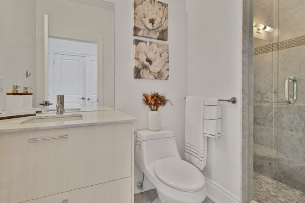 Bright beige bathroom with flower paintings, towels, and flower vase on toilet