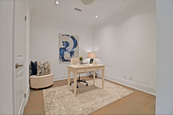 Small desk in room with a ottoman and pillows and abstract painting on the wall