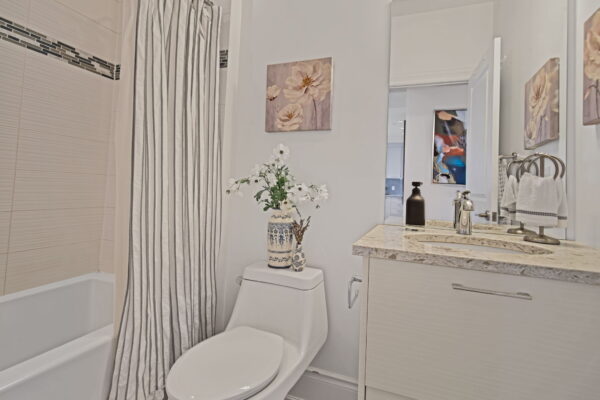 Neutral bathroom with flowers on toilet and flower painting above, mirror, and sink