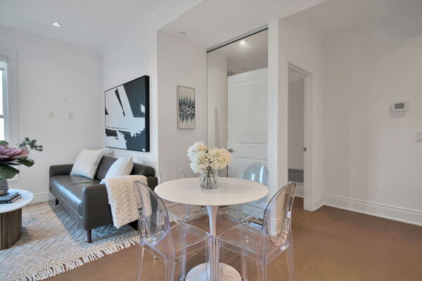 White round dining table with flowers on top and clear chairs and black sofa with abrstract painting and glass wall