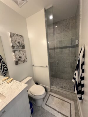 Bathroom with towel and painting on the wall with a standing shower, toilet, and sink