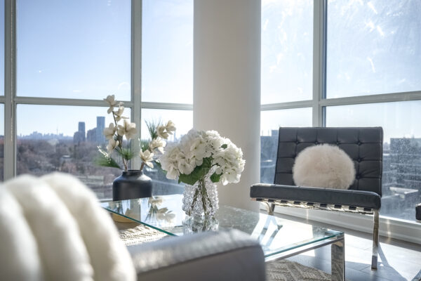 Close up on decor of flowers on glass coffee table and leather sofa and chair with pillow