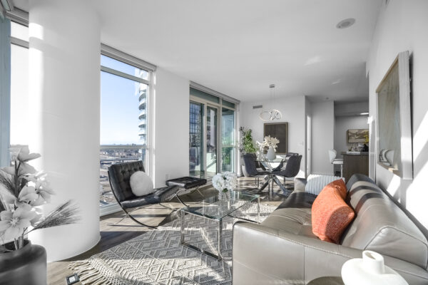 Modern living room with a glass coffee table, grey couch, and black leather chair