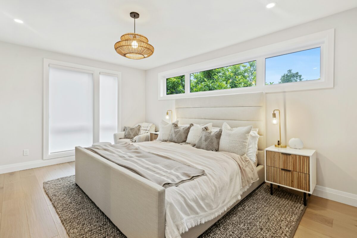 Modern neutral bedroom with upholstered headboard, layered bedding, and large windows.