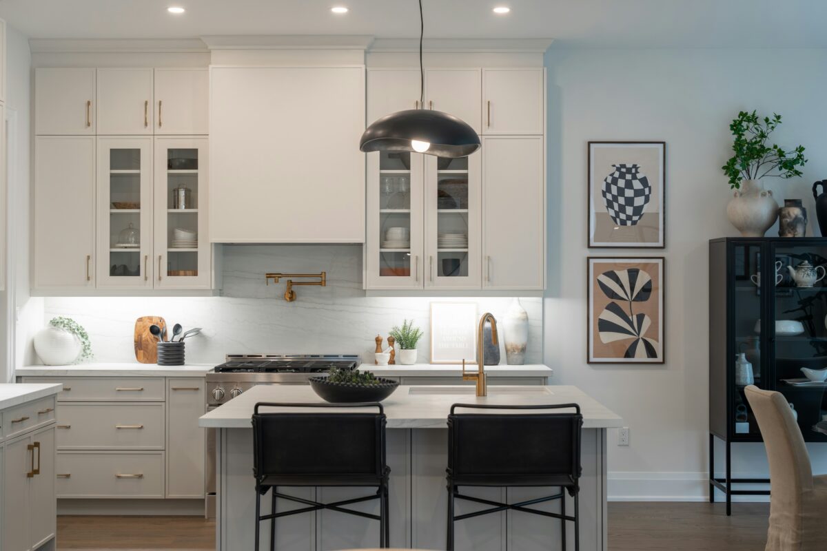 Modern white kitchen with gold accents, marble backsplash, and central island.